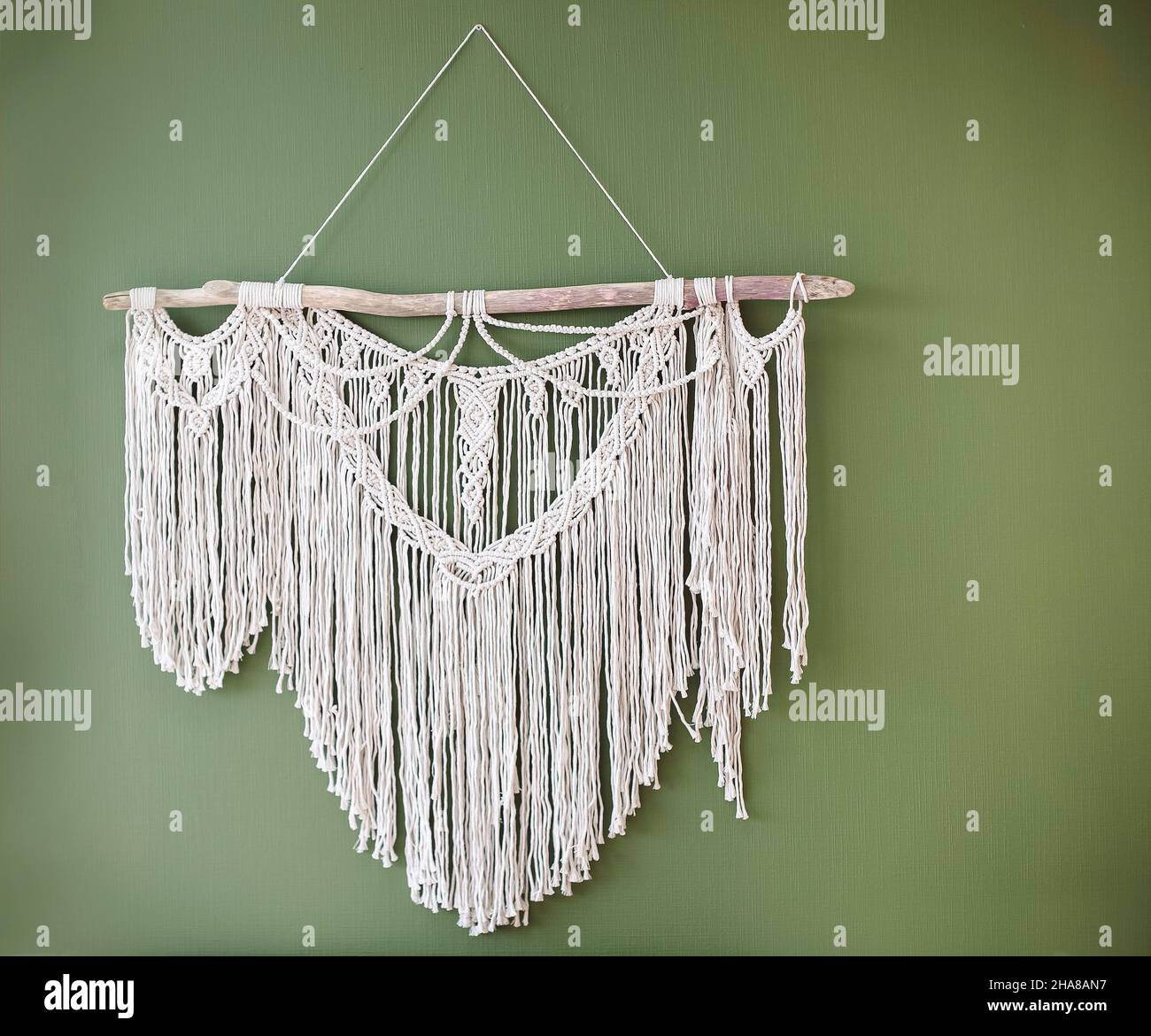 Nahaufnahme Foto von durchbrochenen handgefertigten Macrame Dekoration hängen an der grünen Wand in der Wohnung, aus verschiedenen Arten von Faden, Schnur und Seil, böhmen Stockfoto