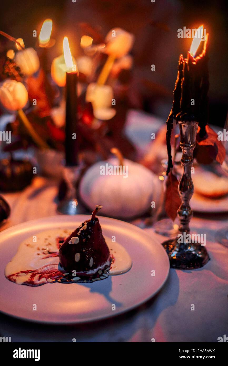 Selektiver Fokus von Birnen-Dessert mit Sabayon, italienische Zabaglione-Sauce auf dem Teller serviert auf dem Esstisch im Halloween-Stil dekoriert, mit schwarzer Kerze Stockfoto
