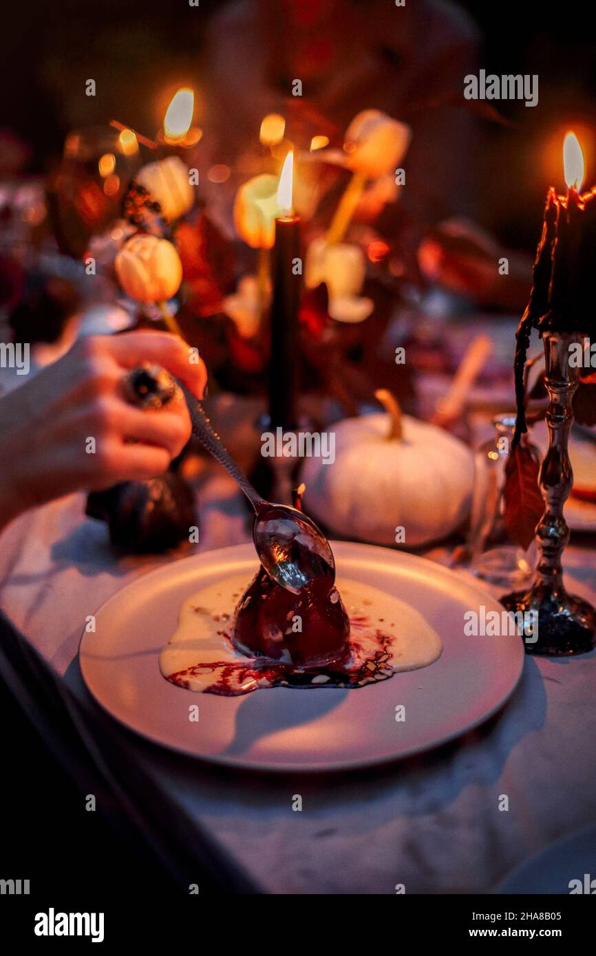 Selektiver Fokus von Birnen-Dessert mit Sabayon, italienische Zabaglione-Sauce auf dem Teller serviert auf dem Esstisch im Halloween-Stil dekoriert, mit schwarzer Kerze Stockfoto