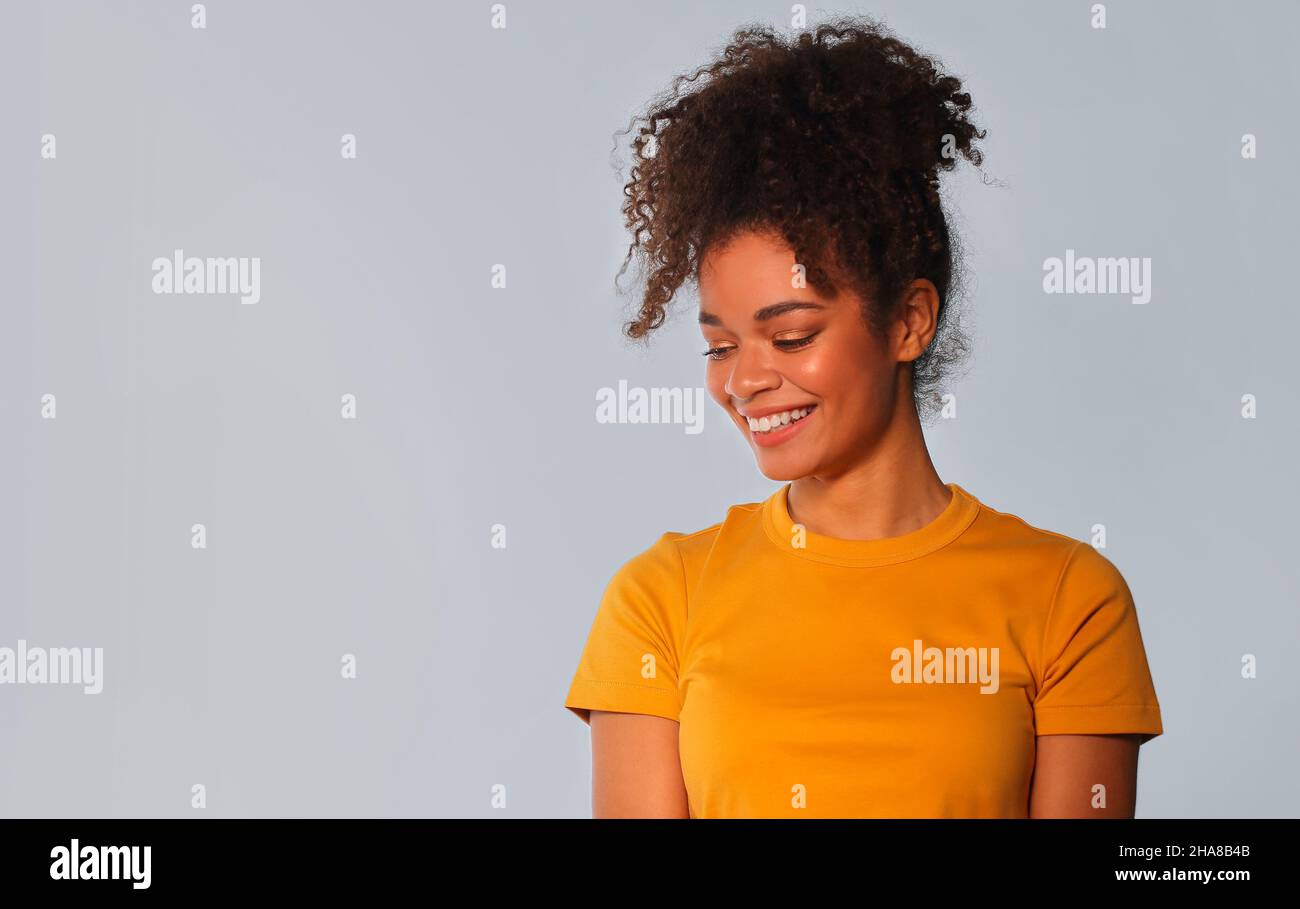 Überfröhliche afroamerikanische Frau in hellgelbem T-Shirt mit lockigen Haaren lachend in die Kamera schauend, ihre weißen glatten Zähne zeigend, posiert gegen g Stockfoto