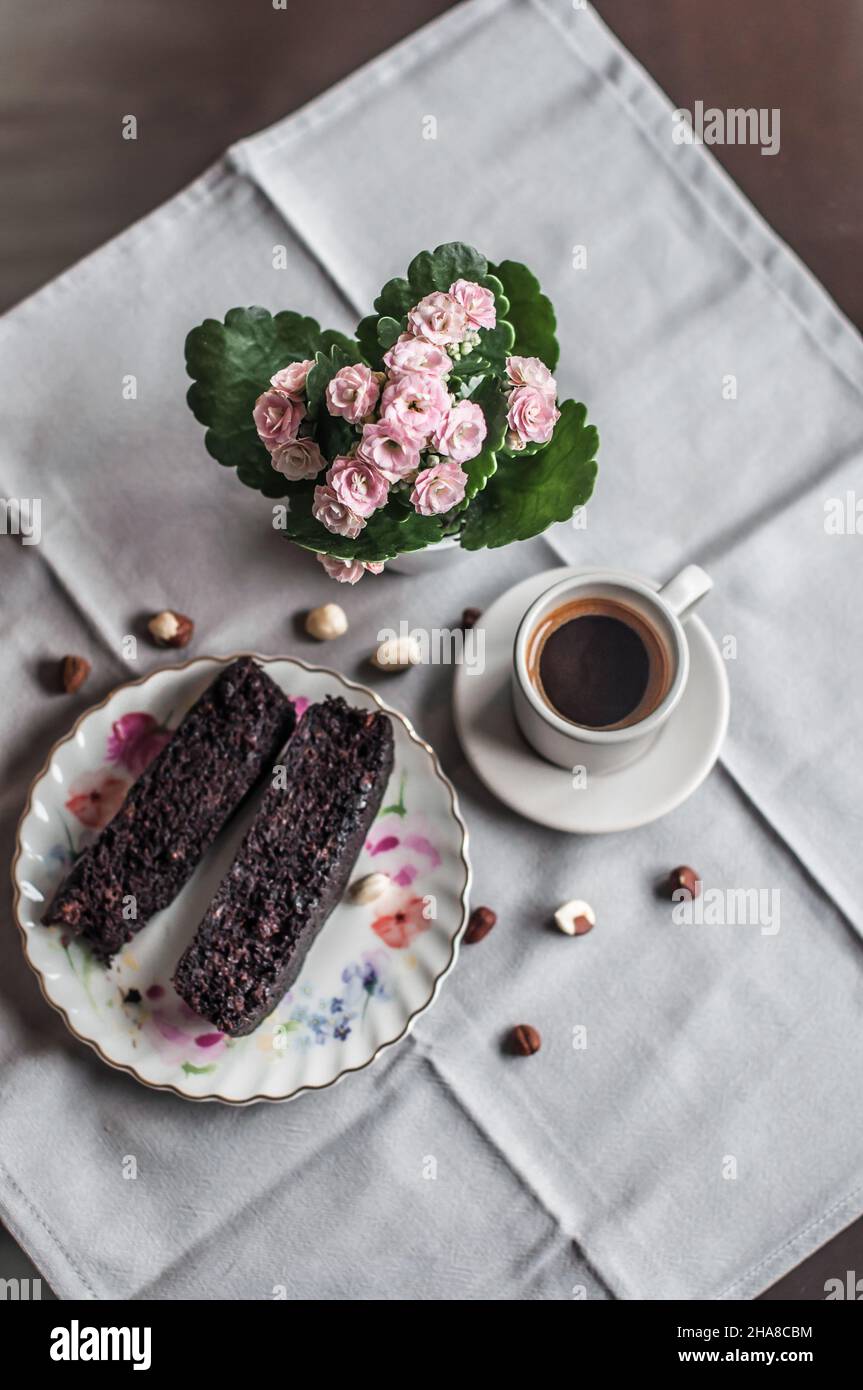 Schokoladenkuchen auf einem Teller mit Muster, eine Tasse Kaffee und Kalanchoe. Stockfoto
