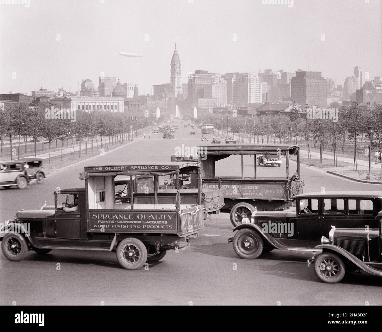 1920S 1930S AUTO- UND LKW-VERKEHR RUND UM DAS ART MUSEUM BLICK IN RICHTUNG DOWNTOWN SKYLINE BLIMP IN SKY PHILADELPHIA PA USA - P2881 HAR001 HARS STRUKTUREN AUTOMOBILE BENJAMIN FRANKLIN PARKWAY STÄDTE KEYSTONE STATE VEHICLES LUFTSCHIFF GEBÄUDE DIRIGIBLE SCHWARZ-WEISSE STADT DER BRÜDERLICHEN LIEBE HAR001 ALTMODISCH Stockfoto