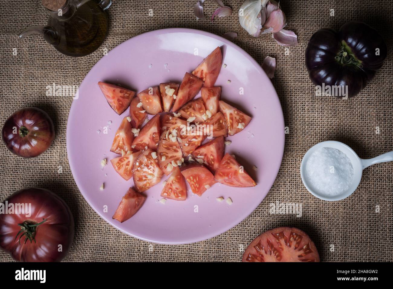 Tomate der Sorte Mar Azul, gehackt und salatgekleidet, begleitet von Knoblauch, Salzflocken, Pfeffer, Öl und ganzen Tomaten. Stockfoto