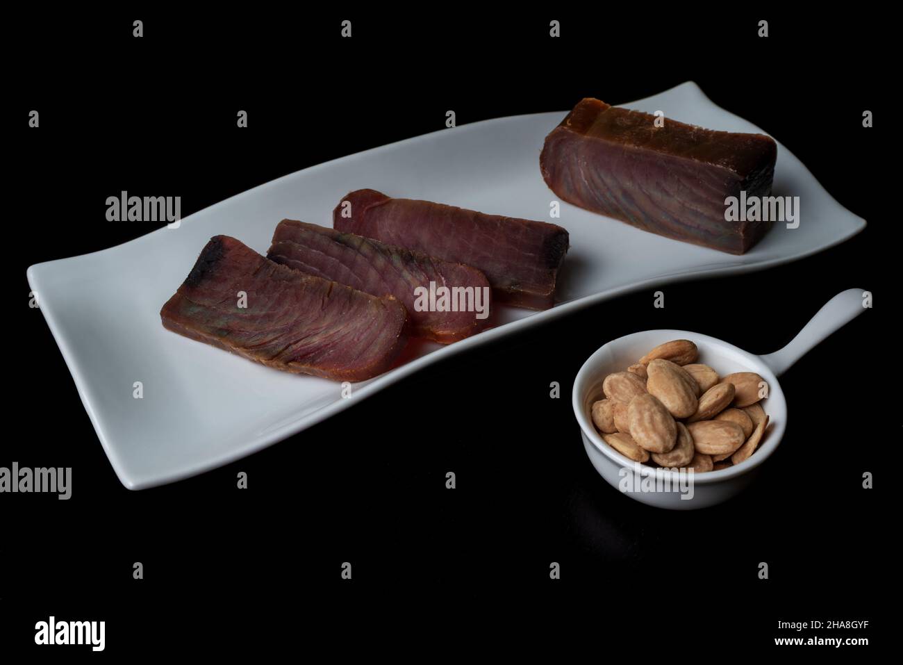 Mehrere Stücke Thunfisch-Ruck (mojama) auf einem Teller, begleitet von gesalzenen Mandeln. Stockfoto