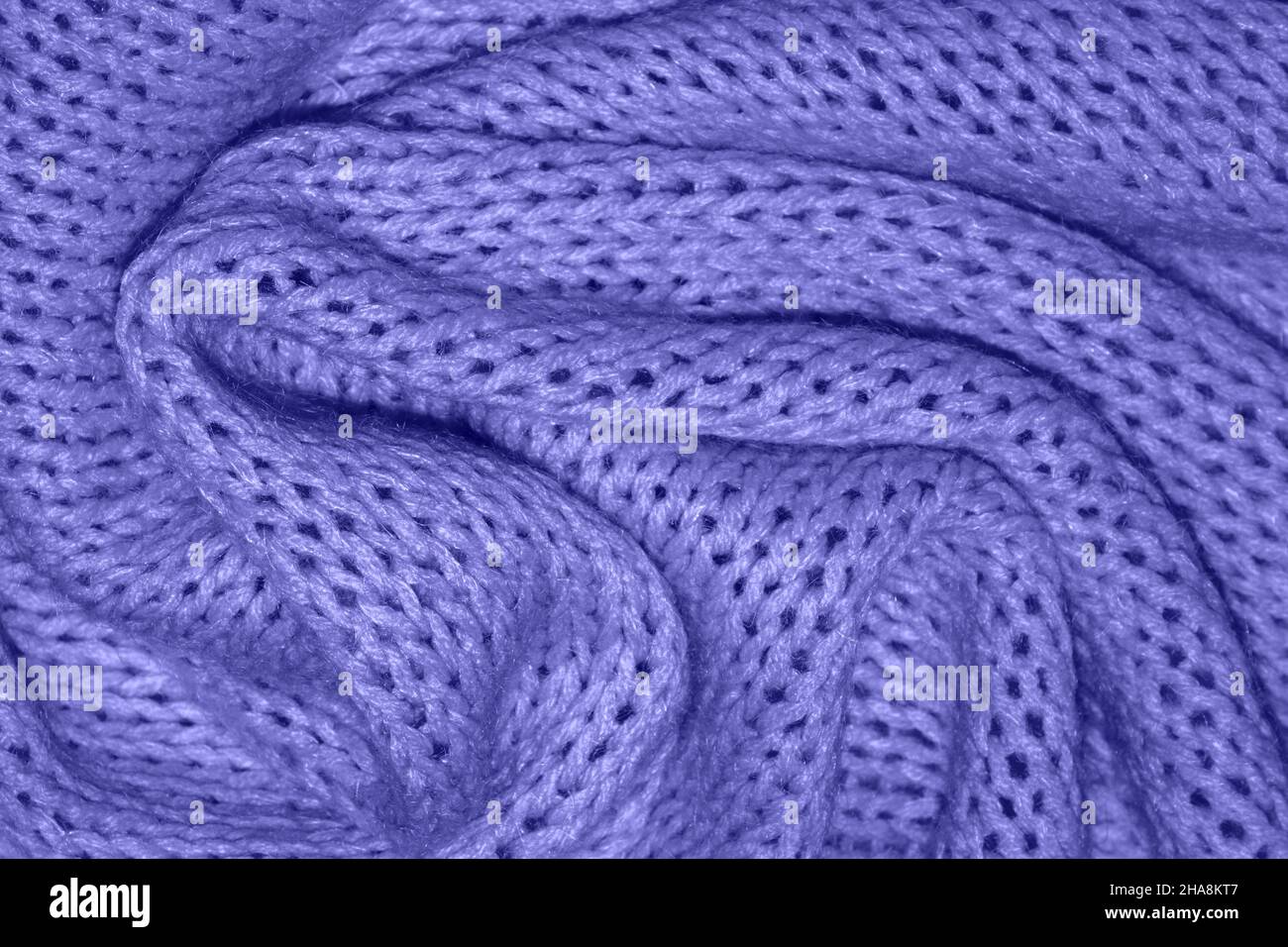 Sehr schöne Textur eines warm gestrickten lila Pullovers mit Falten. Zöpfe im Muster, weicher Fokus. Flaches Design, Nahaufnahme. Aufnahmen mit weichem Fokus in Schwarzweiß. Speicherplatz kopieren. Die modische Farbe von 2022. Sehr perifarbener Hintergrund. Stockfoto