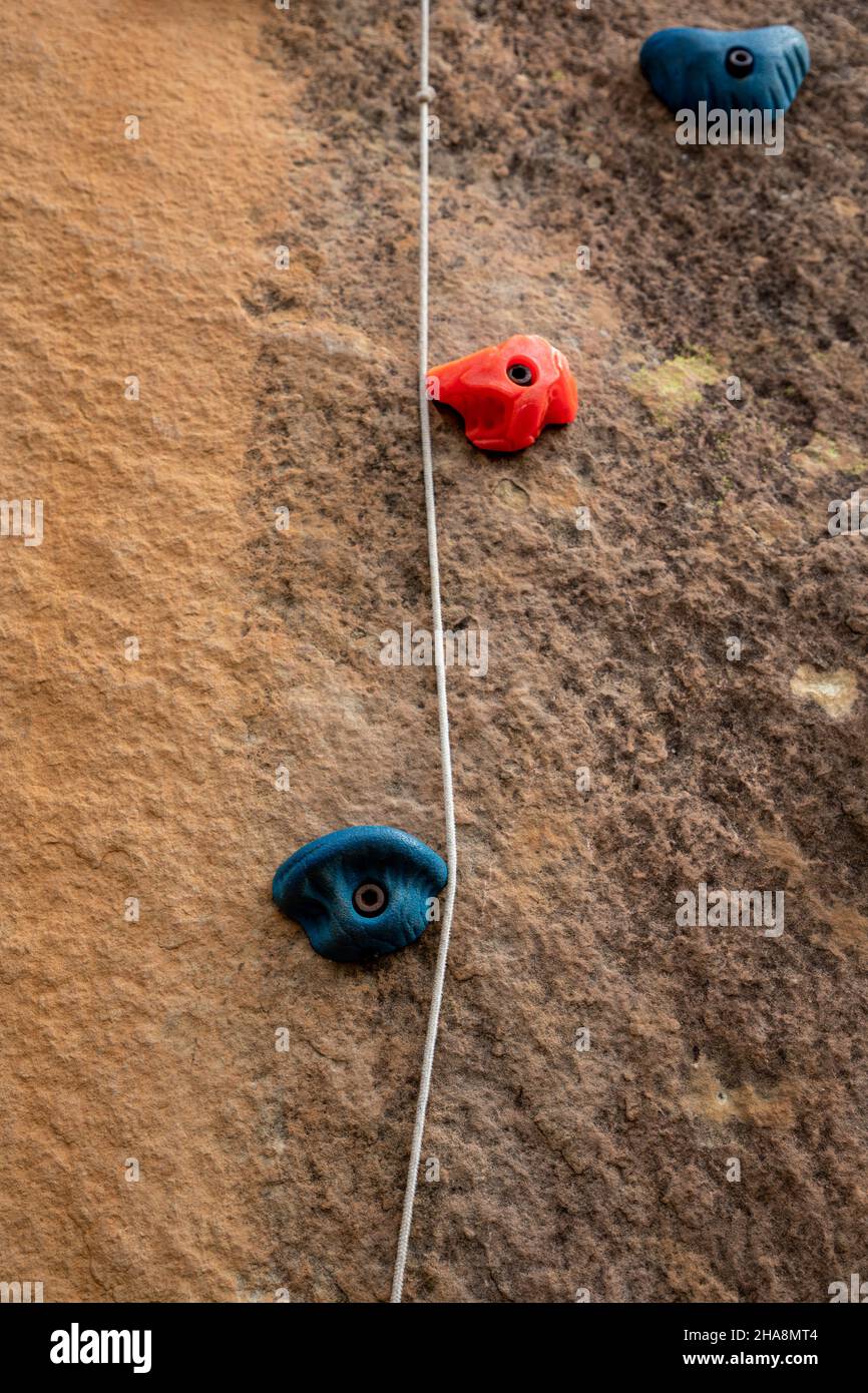 Nahaufnahme eines blauen und eines orangen Kunststoffgriffs, der beim Klettern verwendet wird und in einer Felswand verankert ist. Stockfoto