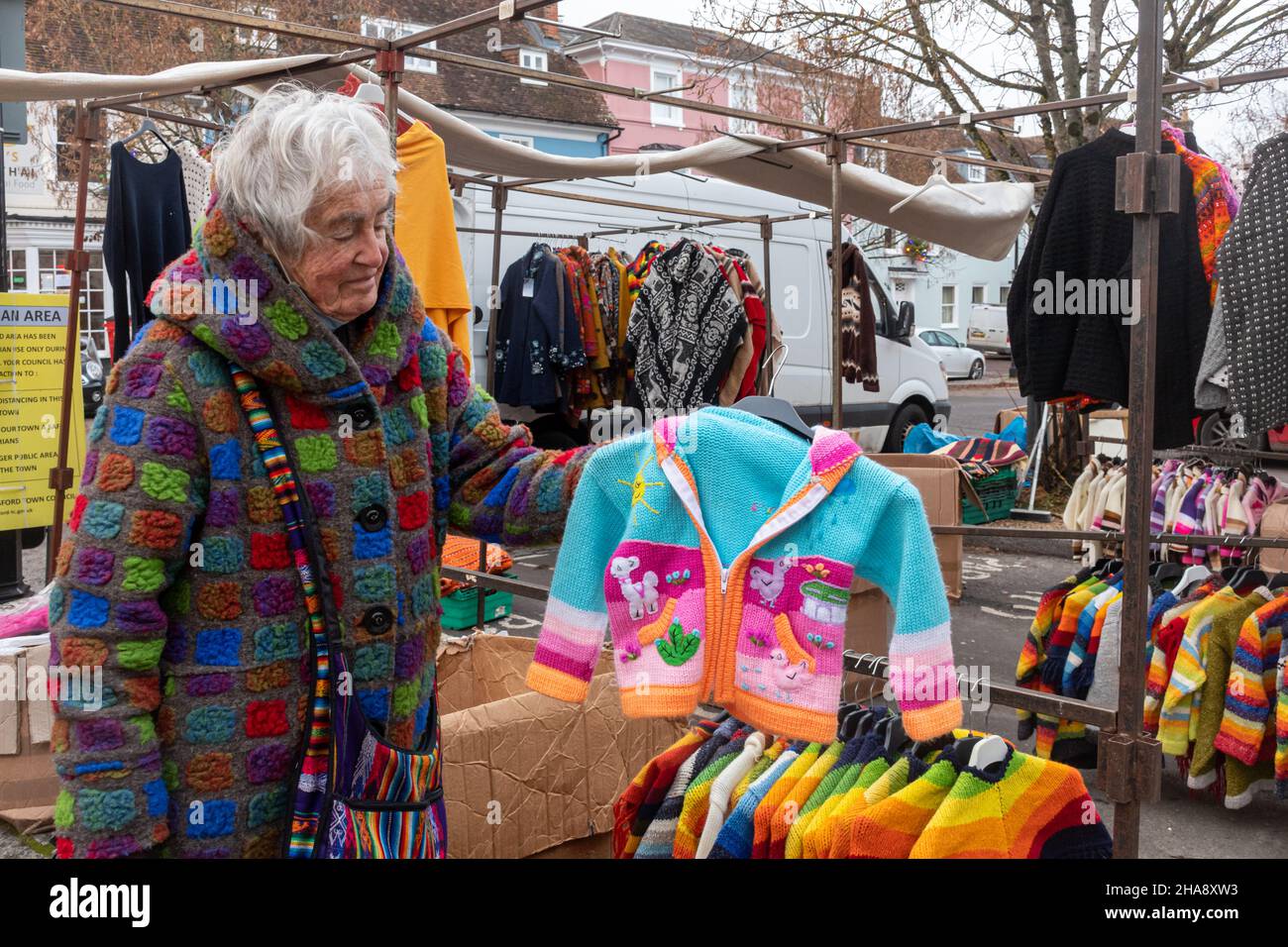 Eine ältere Frau, die an einem Marktstand arbeitet, der handgefertigte Wolljacken, Pullover, Strickjacken, UK in leuchtenden Farben verkauft. Marktanbieter. Stockfoto