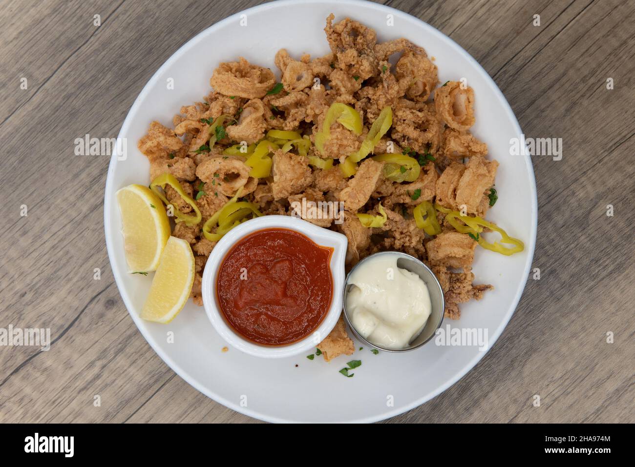 Blick von oben auf eine knackige Schüssel voller zerschlagener Calamari-Ringe, gemischt mit Paprika, Torte und Cocktailsauce. Stockfoto