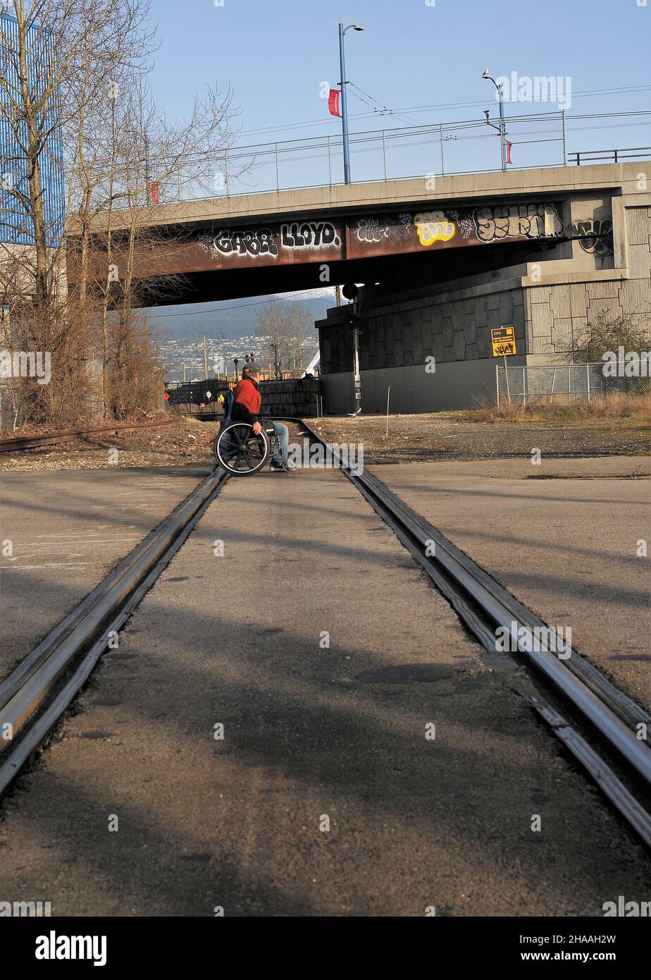 Behinderter Mann im Rollstuhl, der Bahngleise überquert, East Vancouver, British Columbia, Kanada. Stockfoto