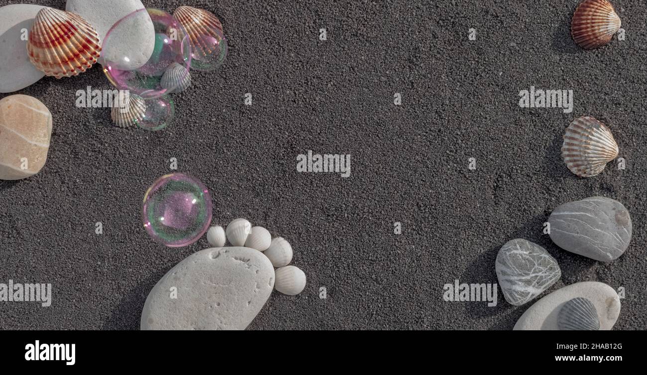 Hintergrund Seesandkörner. Platz für Text. Kieselsteine in Form eines kleinen Fußes, um eine Geburt anzukündigen. Stockfoto