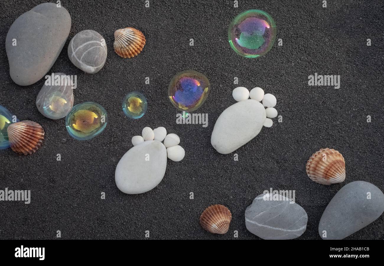 Hintergrund Seesandkörner. Platz für Text. Kieselsteine in Form eines kleinen Fußes, um eine Geburt anzukündigen. Stockfoto
