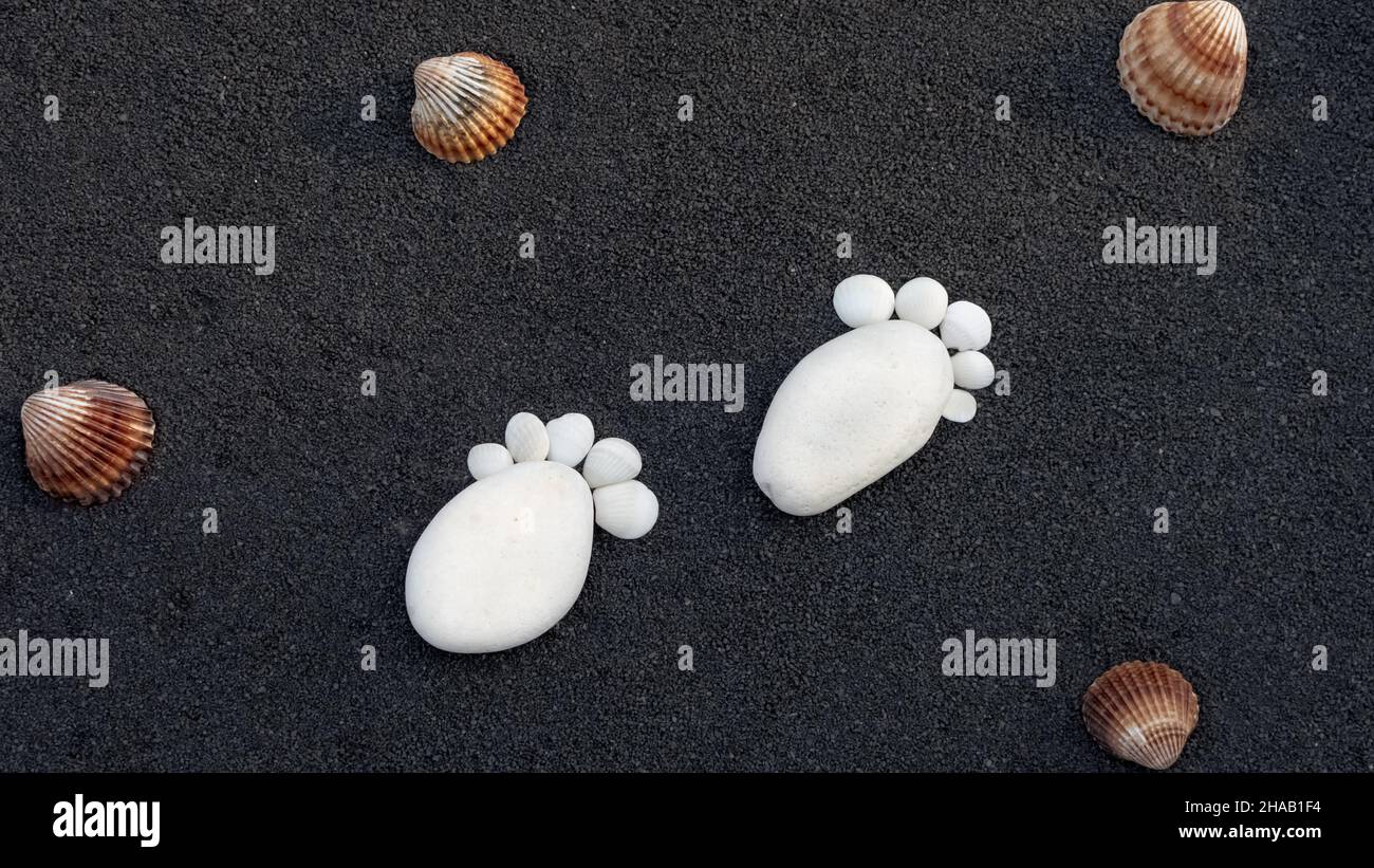 Hintergrund Seesandkörner. Platz für Text. Kieselsteine in Form eines kleinen Fußes, um eine Geburt anzukündigen. Stockfoto