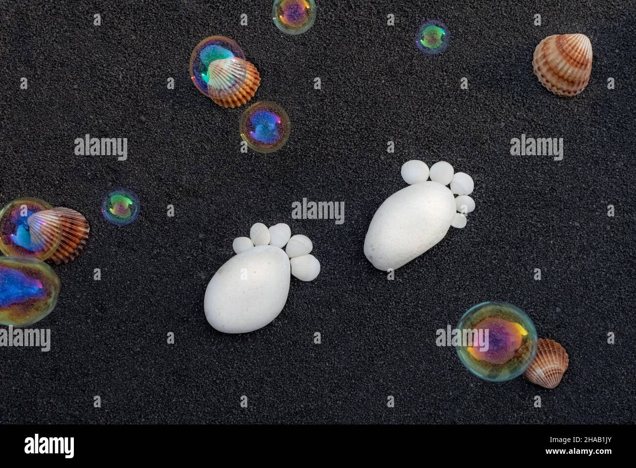 Hintergrund Seesandkörner. Platz für Text. Kieselsteine in Form eines kleinen Fußes, um eine Geburt anzukündigen. Stockfoto