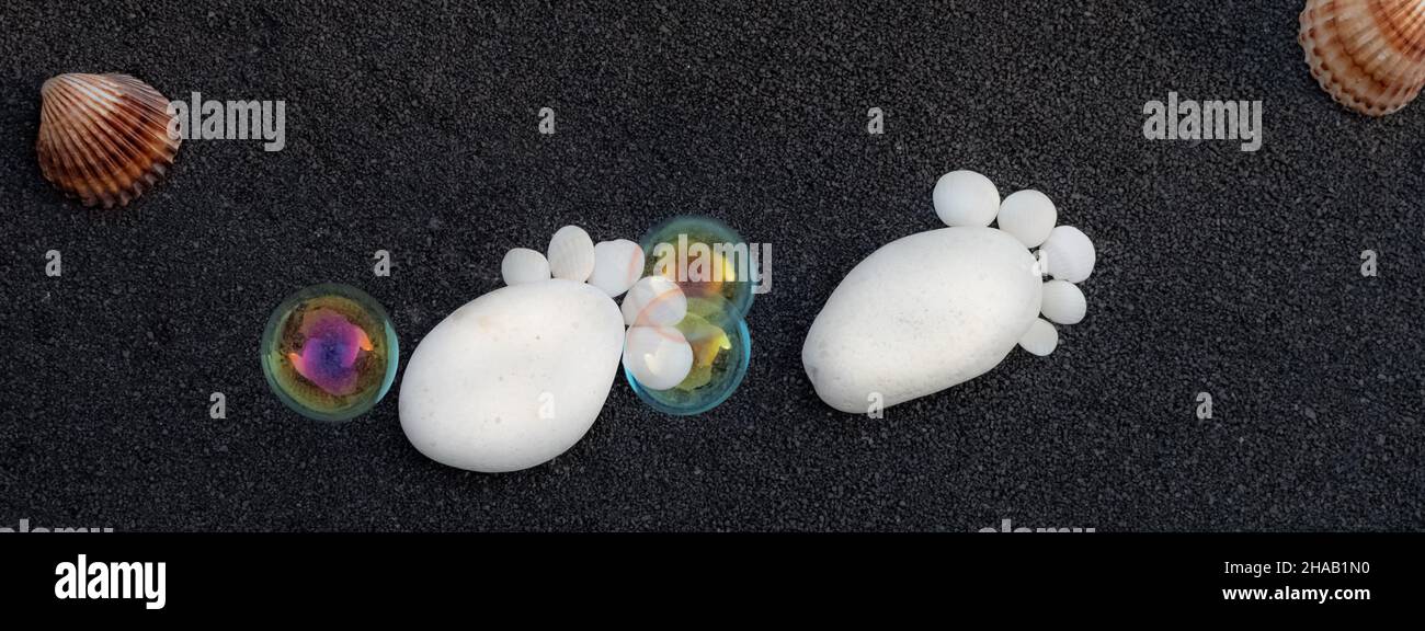 Hintergrund Seesandkörner. Platz für Text. Kieselsteine in Form eines kleinen Fußes, um eine Geburt anzukündigen. Stockfoto