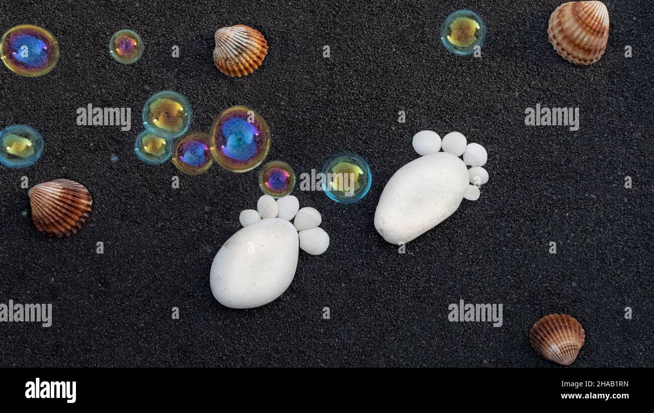 Hintergrund Seesandkörner. Platz für Text. Kieselsteine in Form eines kleinen Fußes, um eine Geburt anzukündigen. Stockfoto