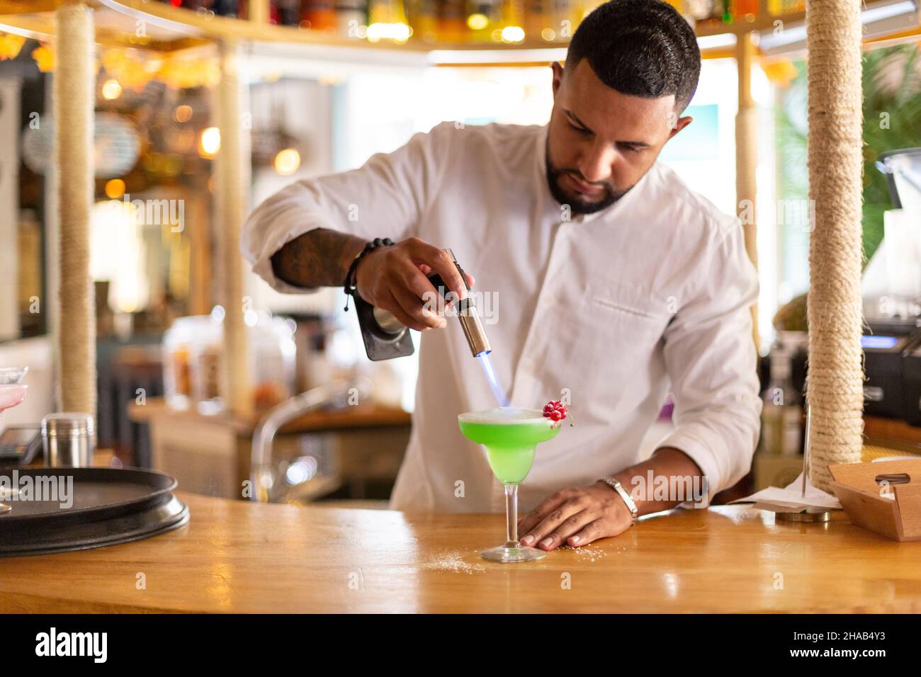 Eleganter junger lateinamerikanischer Kellner, der in einem modernen Restaurant sorgfältig ein alkoholisches Getränk zubereitete. Platz für Text. Selektiver Fokus. Stockfoto