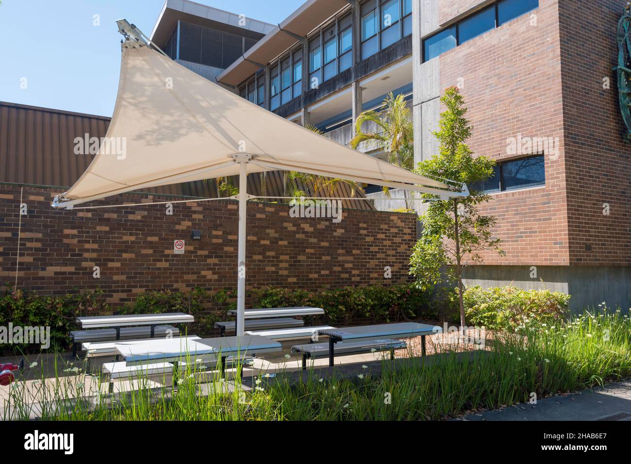 Ein großes, zentral unterstütztes Schattensegel, das einen Ess- und Sitzbereich im Freien auf dem Campus der Macquarie University, Sydney, Australien, abdeckt Stockfoto