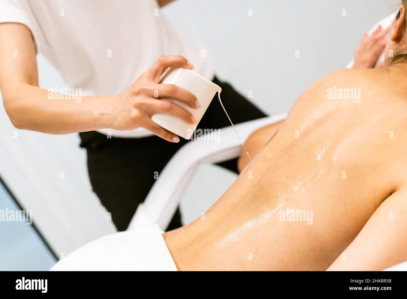 Der professionelle Schönheitssalon gießt Öl aus einer Massagekerze auf den Rücken seines Patienten. Stockfoto