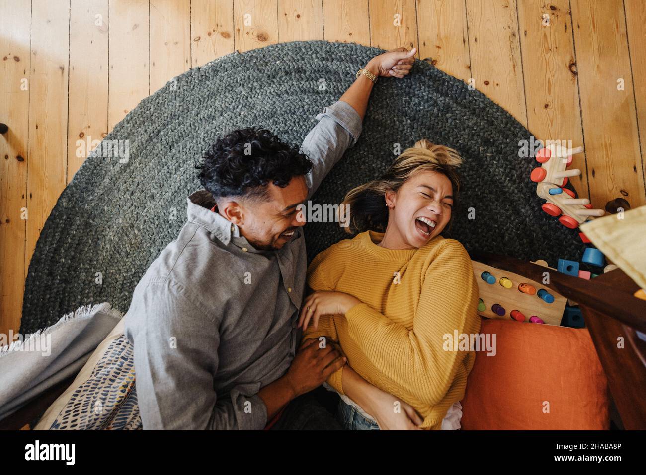 Blick aus der Perspektive eines Ehepaares, das fröhlich lacht, während es im Spielbereich ihrer Kinder liegt. Zwei junge Eltern, die zu Hause Spaß miteinander haben. Stockfoto