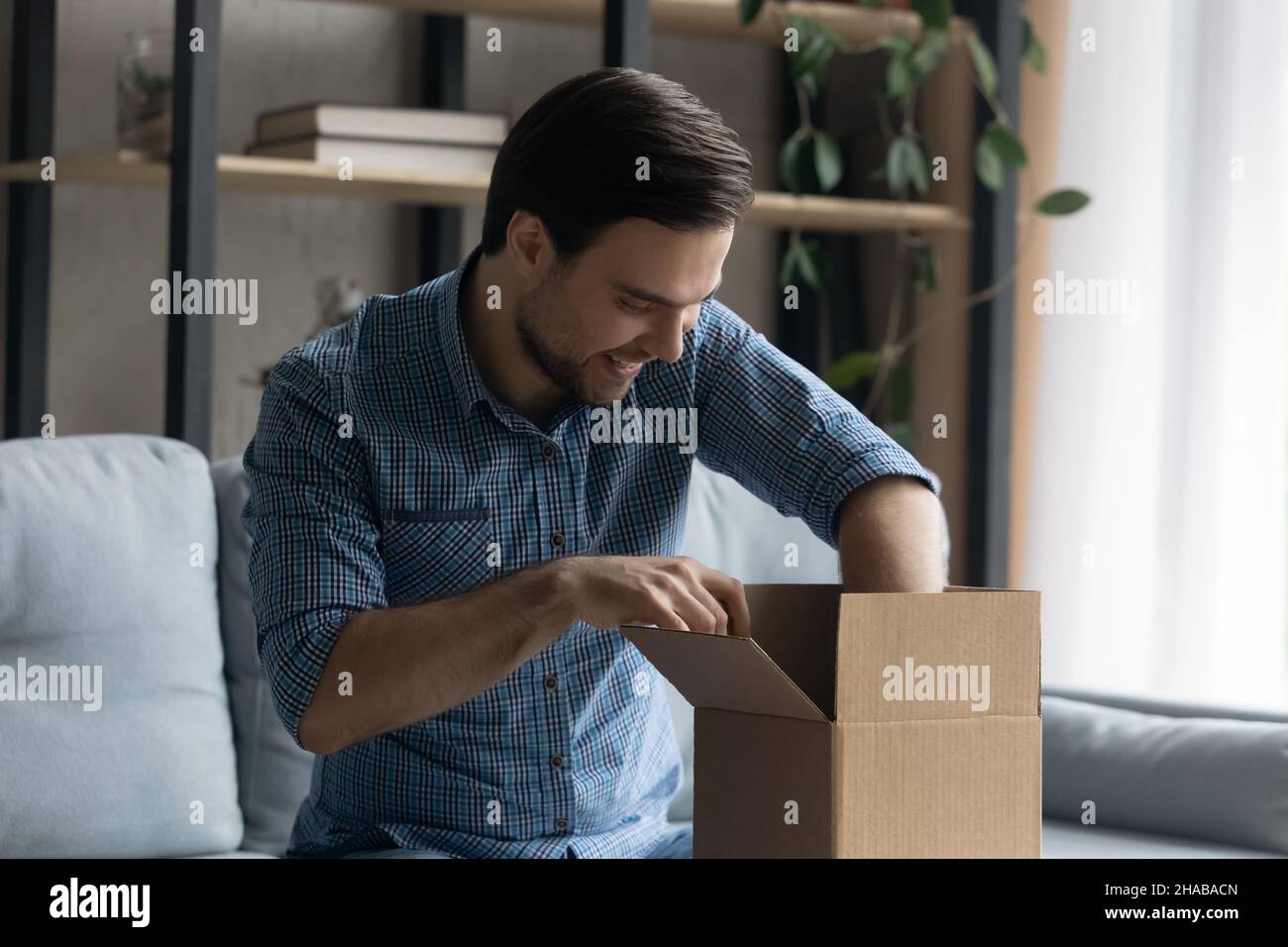 Der Mann, der das gelieferte Paket öffnet, fühlt sich mit dem Online-Kauf zufrieden Stockfoto