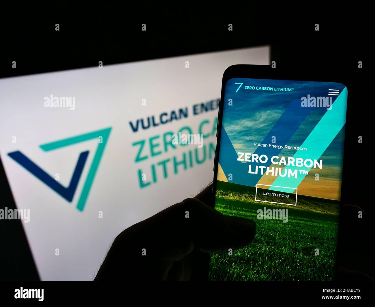 Person mit Mobiltelefon auf der Website des australischen Unternehmens Vulcan Energy Resources Ltd. Auf dem Bildschirm mit Logo. Konzentrieren Sie sich auf die Mitte des Telefondisplays. Stockfoto
