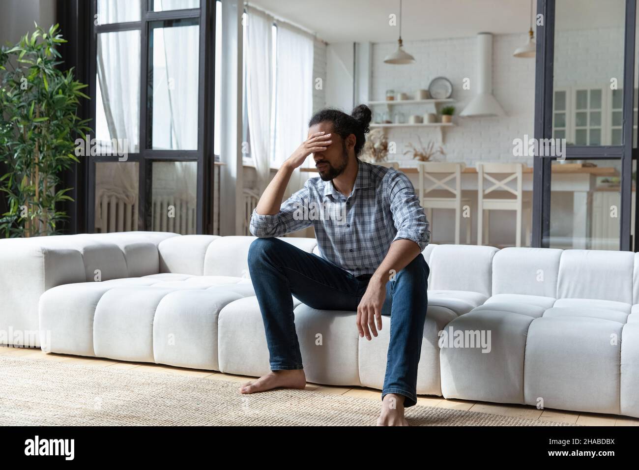 Afrikanischer Kerl sitzen auf Sofa Touch Kopf sieht verzweifelt Stockfoto