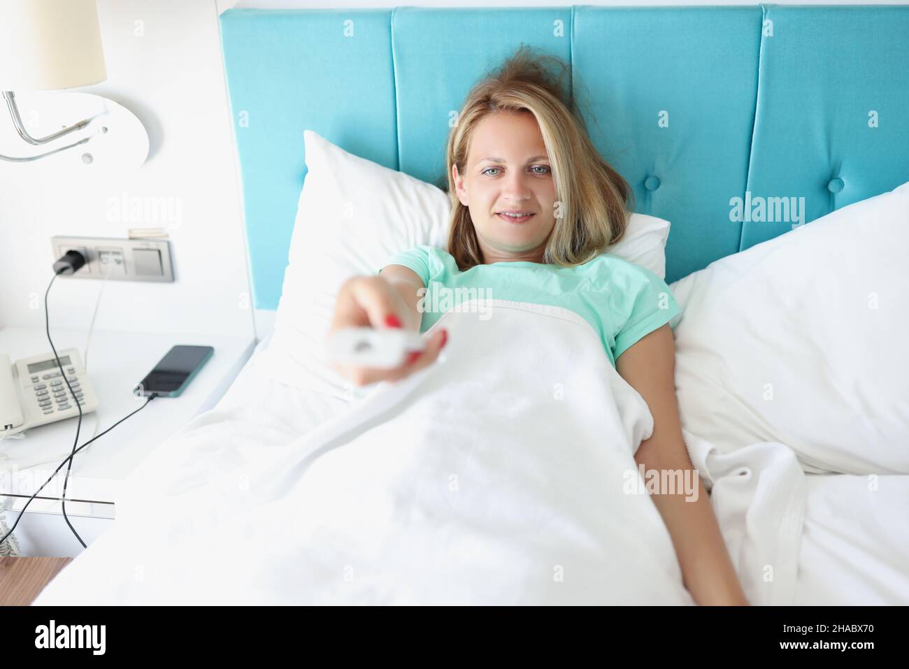 Glückliche Frau, die im Bett lag und mit der Fernbedienung den Sender im fernseher gewechselt hat Stockfoto