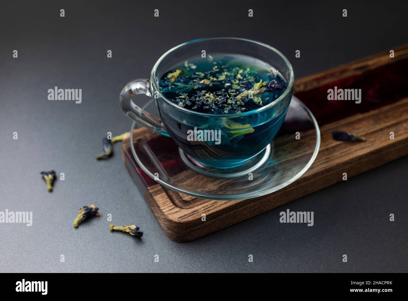 Anchan blauer Thai-Tee in einer transparenten Glasschale mit Teeblättern. Heißes aromatisches Getränk aus Asien auf einem Holzbrett mit getrockneten Blumen Stockfoto