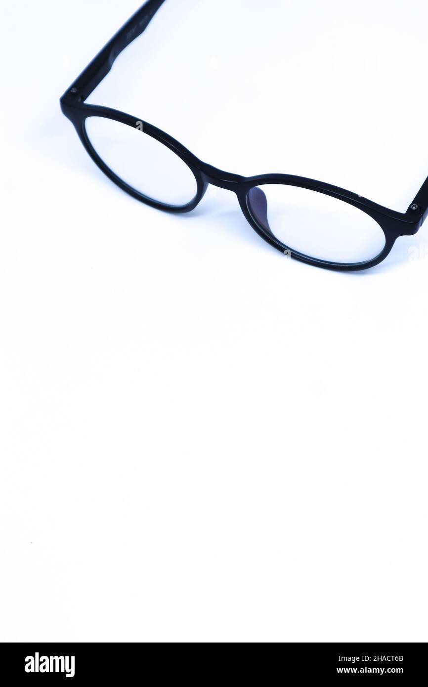 Schräge Top-Aufnahme schwarzer Brillen in der Ecke des minimalistischen weißen Hintergrunds, Portrait-Modus Stockfoto