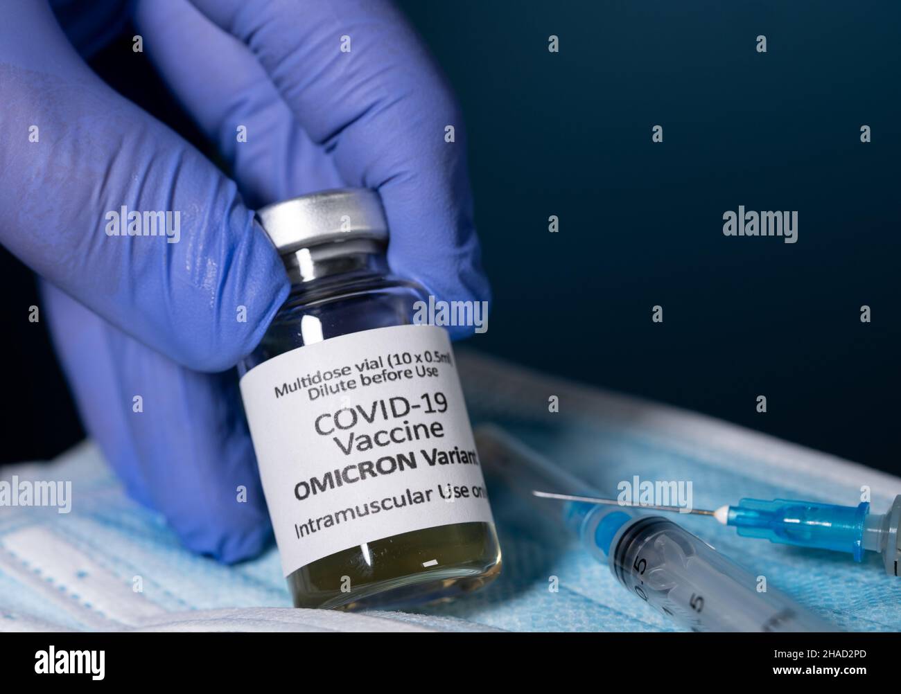 Covid-19-Coronavirus-Impfstoff entwickelt für Omicron-Variante, mit Handschuhen gehalten, mit hypodermischer Spritzennadel und neuen Spritzen im Hintergrund Stockfoto