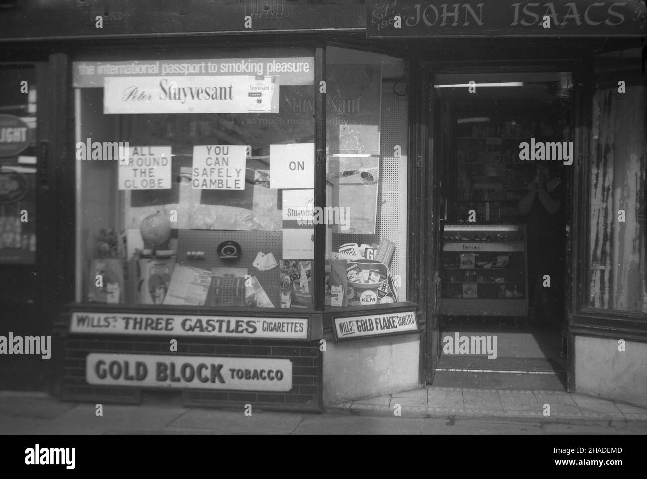 1958, Außenansicht des Schaufensters eines Tabakwarenhandels, John Isaacs, Half Moon Street, Sherborne, Dorset, England, Großbritannien. John Isaacs war ursprünglich Friseur und die Räumlichkeiten zu einer Zeit, kombiniert mit dem Verkauf von Tabak. Im Fenster, Werbung für Peter Stuyvesant Zigaretten, "der internationale Pass zum Rauchvergnügen" und "rund um den Globus, können Sie sicher auf Peter Stuyvesant spielen." Die Marke wurde ‘in Deutschland gegründet und mit ihrer „amerikanischen Mischung“ aus Tabak aus verschiedenen Ländern als international propagiert. Gezeigt wurden auch Wills Three Castles Cigarettes & Gold Block Tabak. Stockfoto 1958, Außenansicht des Schaufensters eines Tabakwarenhandels, John Isaacs, Half Moon Street, Sherborne, Dorset, England, Großbritannien. John Isaacs war ursprünglich Friseur und die Räumlichkeiten zu einer Zeit, kombiniert mit dem Verkauf von Tabak. Im Fenster, Werbung für Peter Stuyvesant Zigaretten, "der internationale Pass zum Rauchvergnügen" und "rund um den Globus, können Sie sicher auf Peter Stuyvesant spielen." Die Marke wurde ‘in Deutschland gegründet und mit ihrer „amerikanischen Mischung“ aus Tabak aus verschiedenen Ländern als international propagiert. Gezeigt wurden auch Wills Three Castles Cigarettes & Gold Block Tabak. Stockfoto