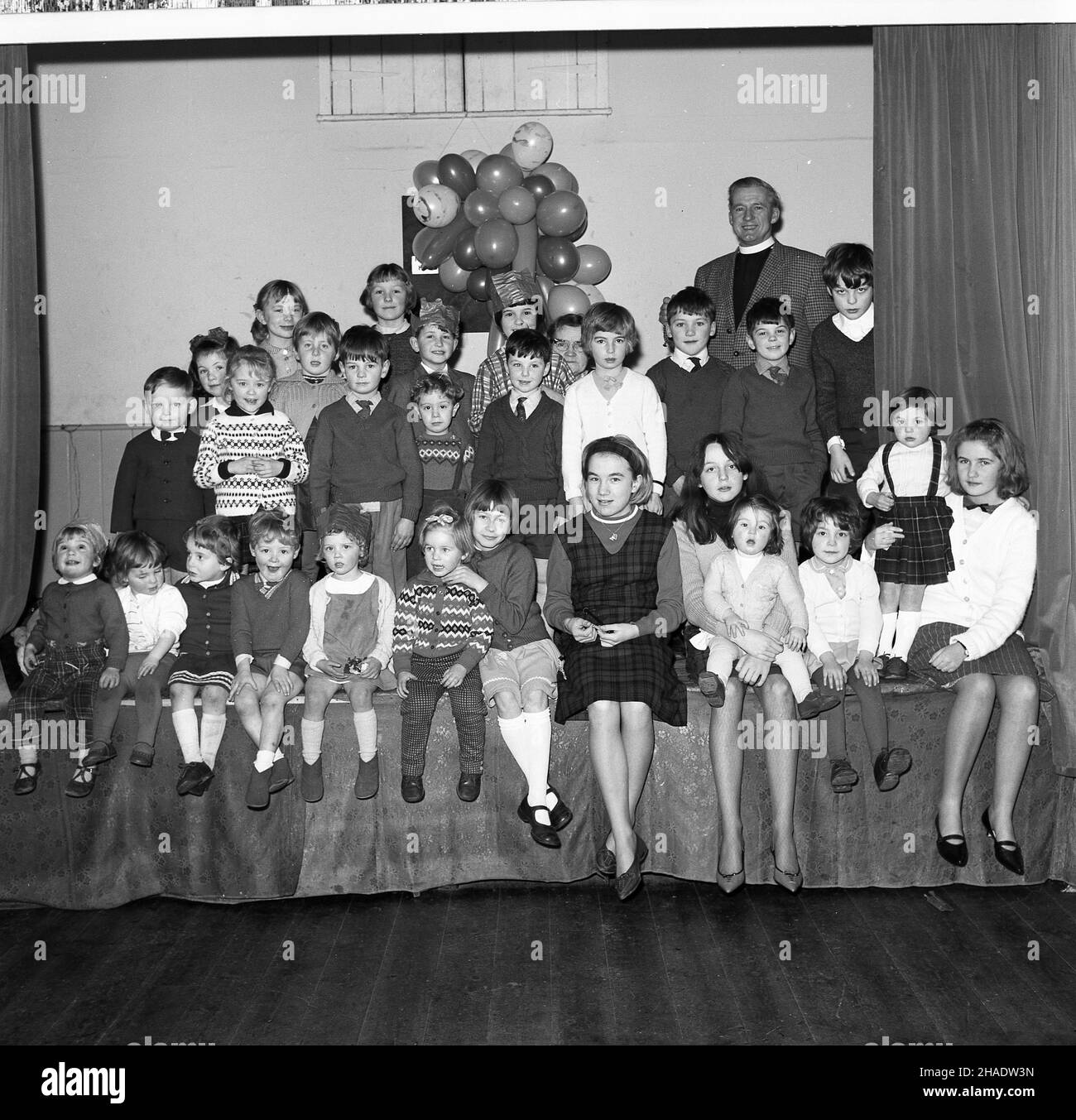 1965, historisch, Gruppe von Kindern, unterschiedlichen Alters, sitzen zusammen auf der Bühne in Longwick Village Hall, Buckiinghamshire, Großbritannien nach der Weihnachtsfeier. Stockfoto