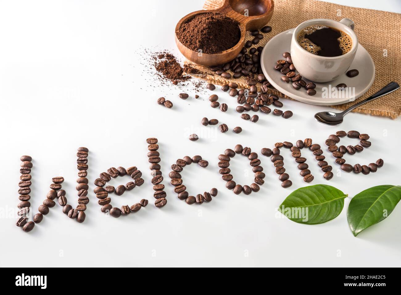 Kaffeetasse und Text aus Kaffeebohnen, isoliert auf Weiß. Text das Wort Willkommen aus Kaffeebohnen. Schrift Stockfoto