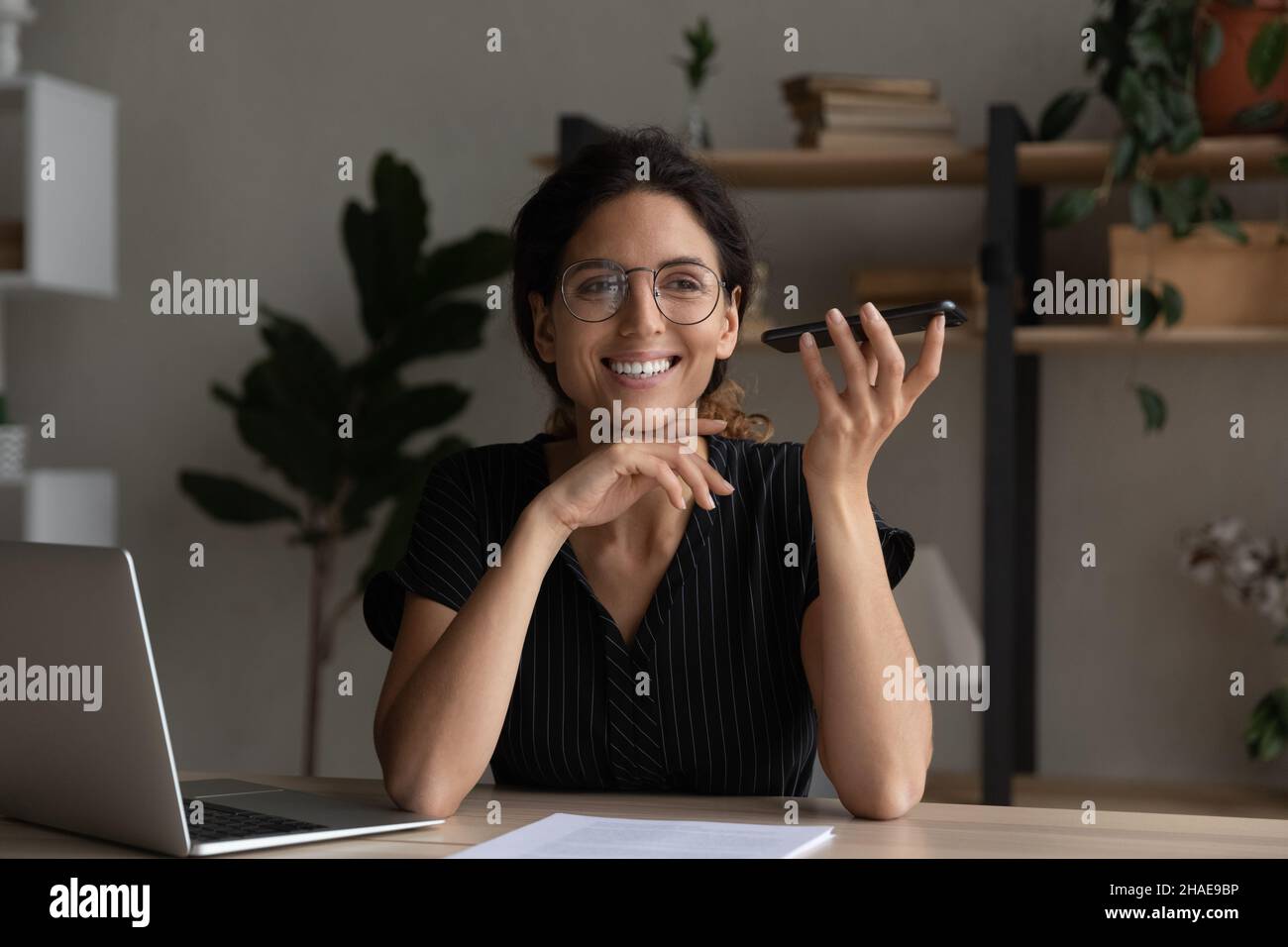 Lächelnde Latino-Frau spricht über Lautsprecher auf dem Smartphone Stockfoto