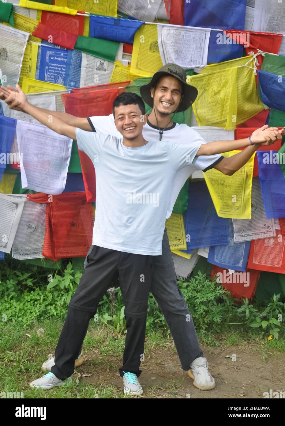 In voller Länge schauten zwei fröhliche männliche Freunde die Kamera an und breiteten die Hände gegen tibetisch-buddhistische Gebetsfahnen aus Stockfoto