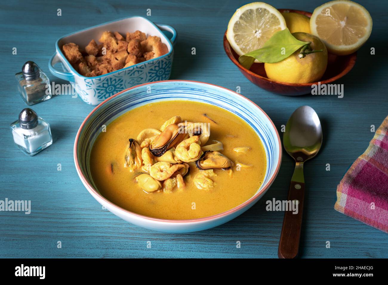 Fischsuppe, basierend auf Garnelen, Muscheln, Muscheln, Seehecht und Tintenfisch, Begleitet von frittierten Brotscheiben auf einem hellblauen Holztisch. Stockfoto