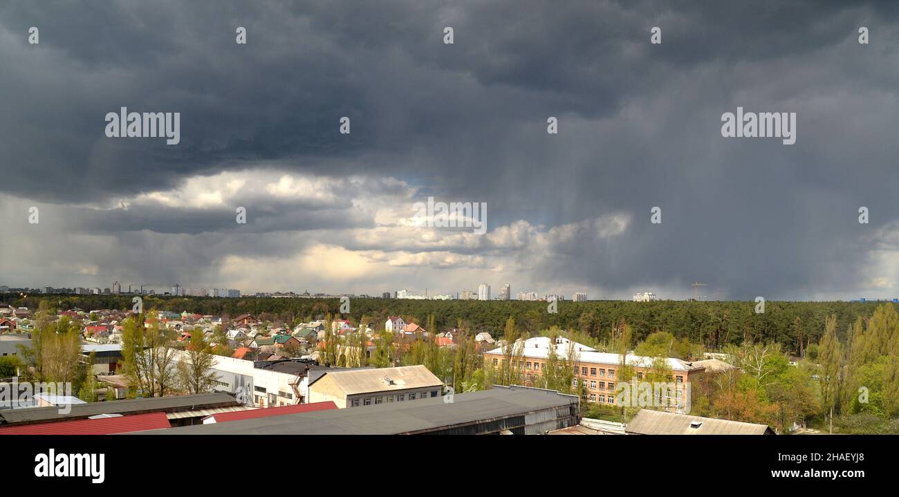 Regensturm über der Stadt, schwere Wolken fliegen über Häuser und Wald, Hurrikan kommt Stockfoto