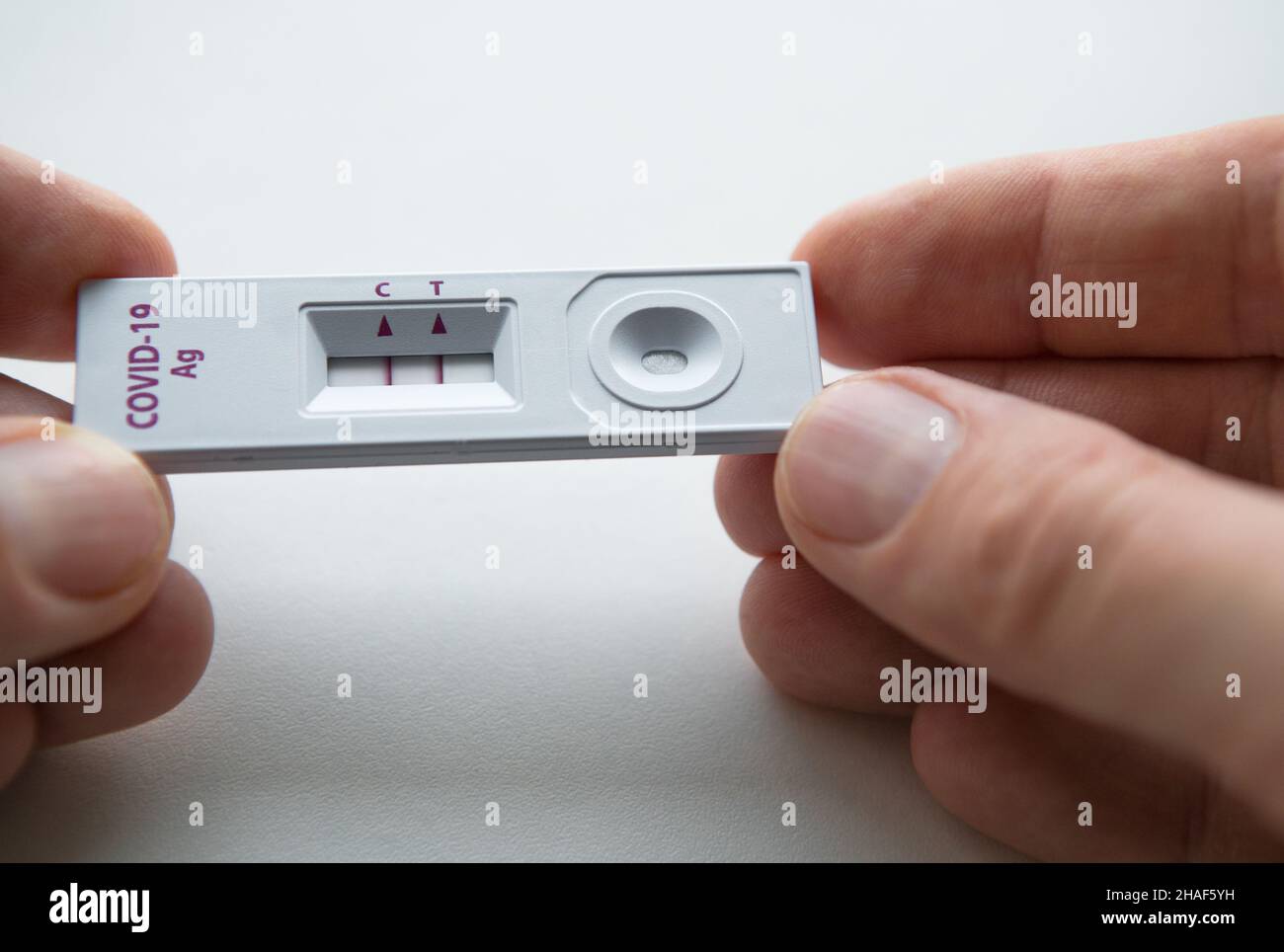 Rapid Antigen Detection Test (RADT) mit zwei roten Streifen, die ein POSITIVES Ergebnis eines Tests mit menschlichen Proben zeigen. Mans Finger halten den weißen Kunststoff d Stockfoto
