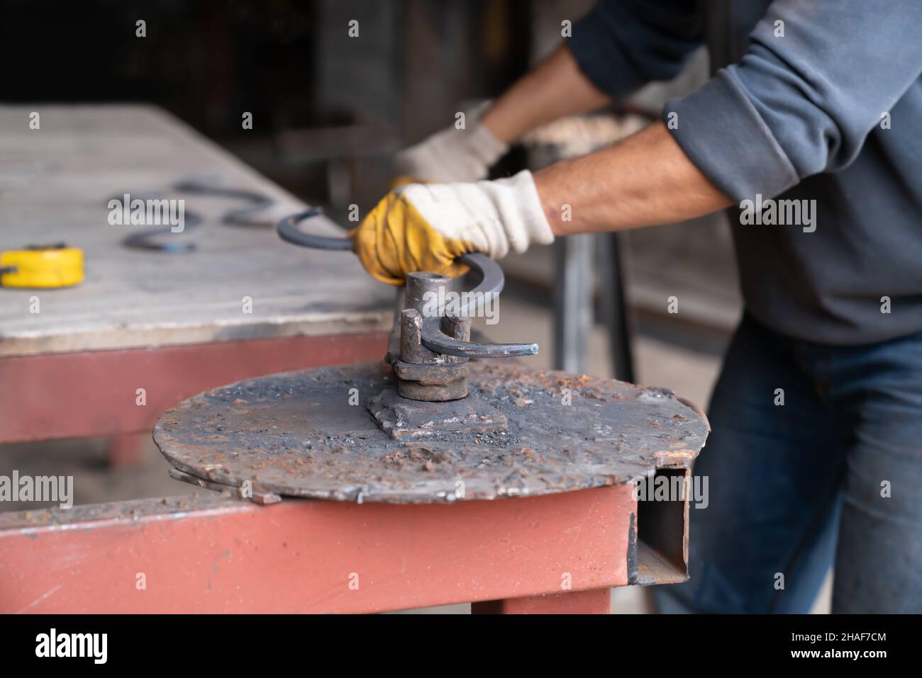 Mann biegt Metallteil Schaffung gekrümmter Form mit einer speziellen Maschine. Schmiede - Metallwerkstatt. Nahaufnahme. Stockfoto