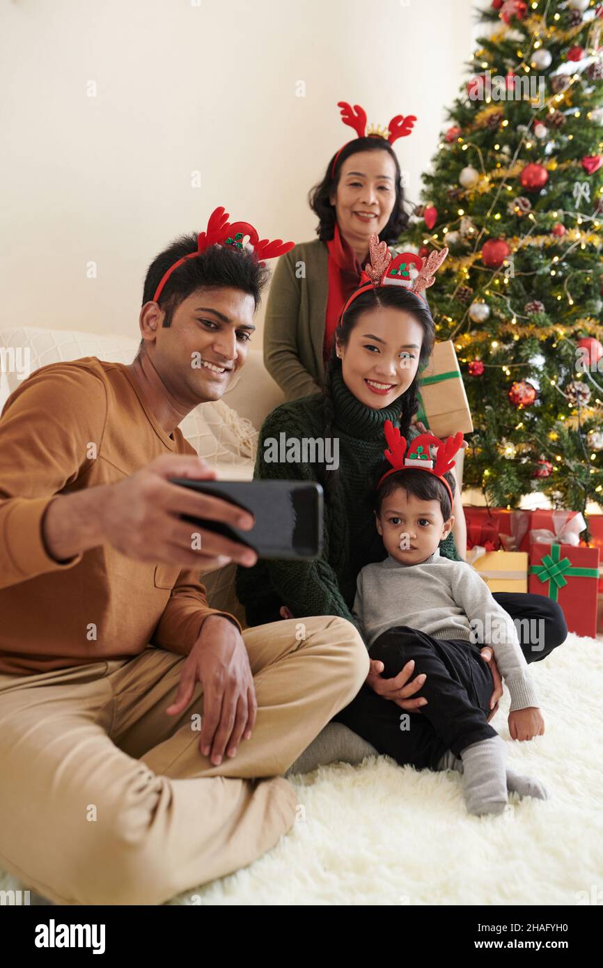 Lächelnder Mann, der mit seiner Familie am geschmückten Weihnachtsbaum zu Hause fotografiert Stockfoto