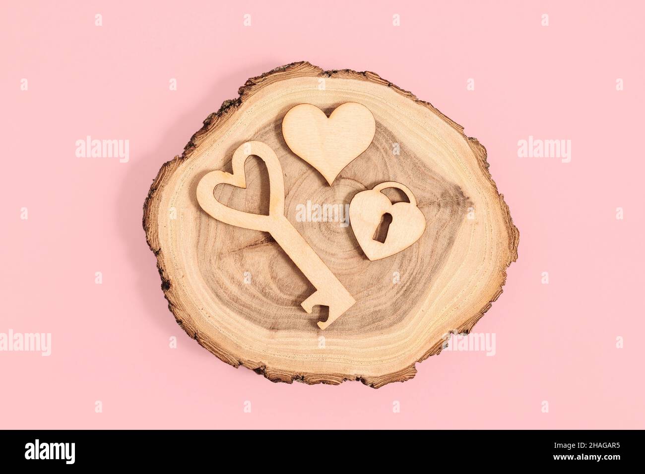 Holzfiguren aus Schloss, Schlüssel und Herz auf rosa Hintergrund. Valentinskarte Stockfoto