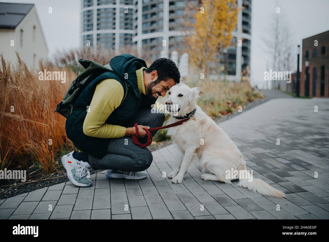 Glücklicher junger Mann, der während eines Spaziergangs im Freien in der Stadt seinen Hund hockt und umarmt. Stockfoto