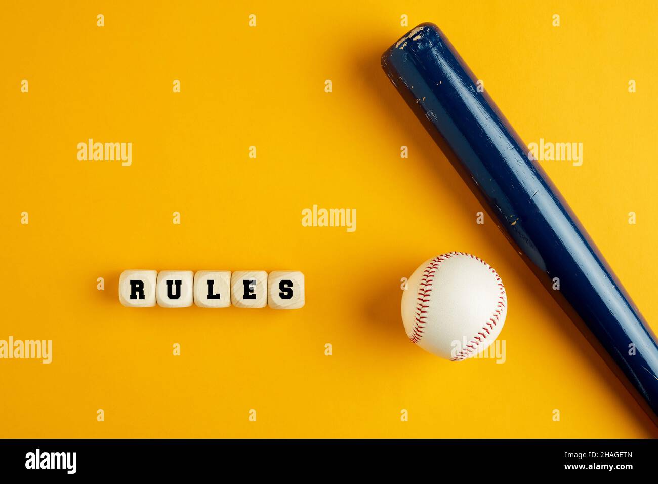 Hölzerner Baseballschläger und ein Ball auf gelbem Hintergrund mit dem Wort rules. Baseballregeln Konzept. Stockfoto