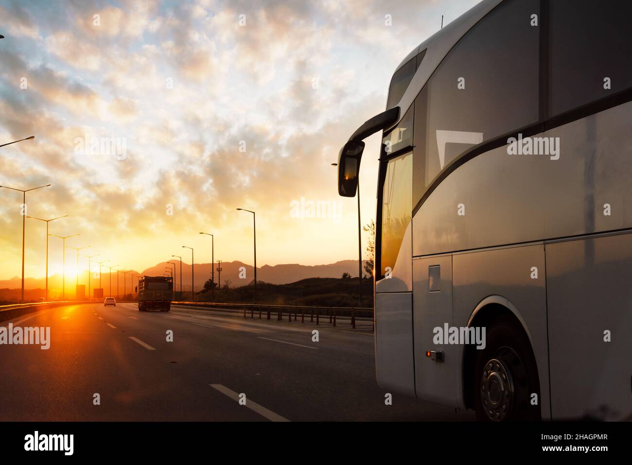 Gegen den Sonnenuntergang fährt ein Bus auf der asphaltierten Landstraße. Reise- und Transportkonzept. Hochwertige Fotos Stockfoto