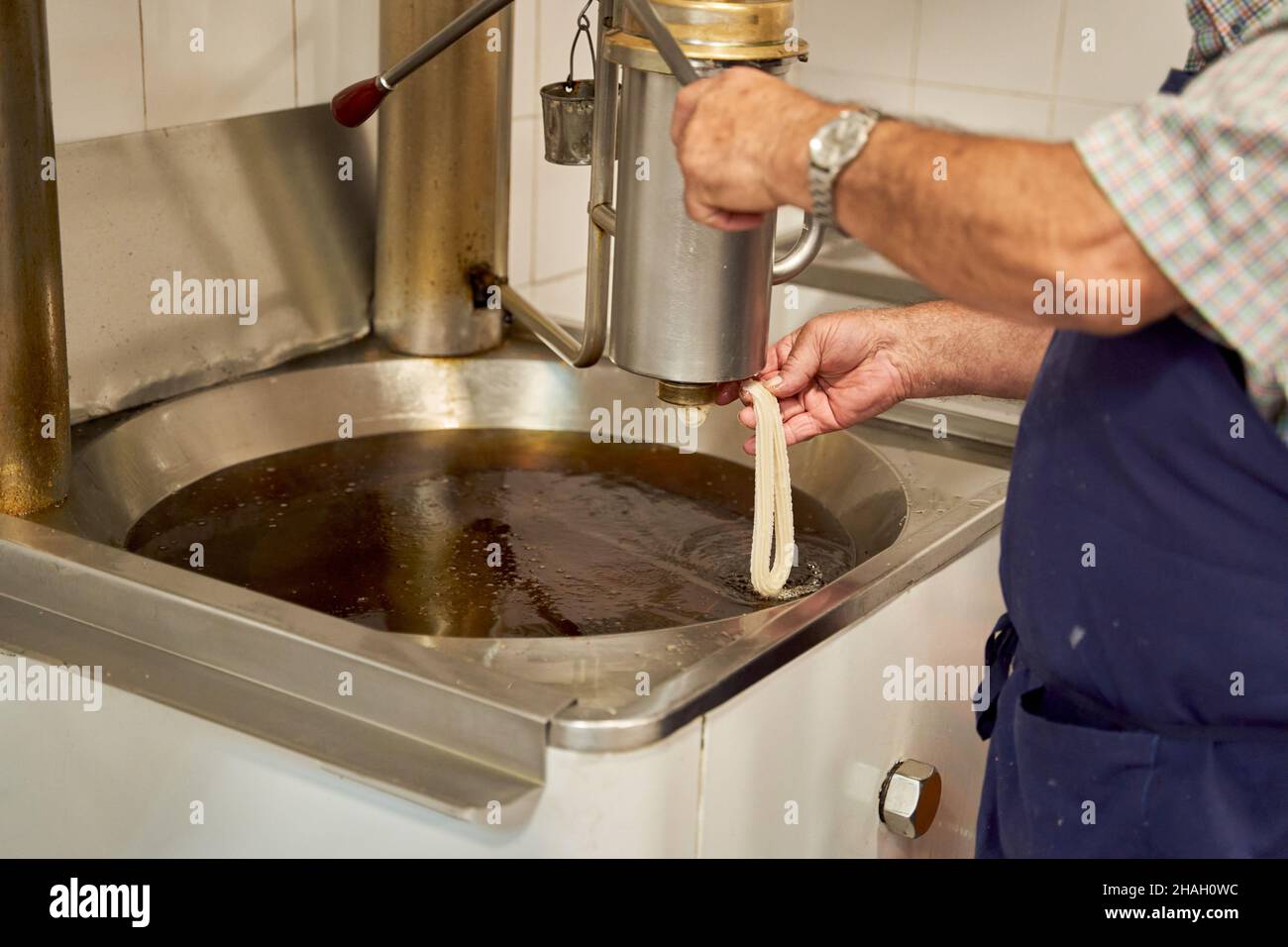 Seitenansicht eines unbekannten Kochs in der Schürze, der rohen Teig in frittiertes Öl gießt, während er Churros, ein typisch spanisches Frühstück, zubereitet. Stockfoto