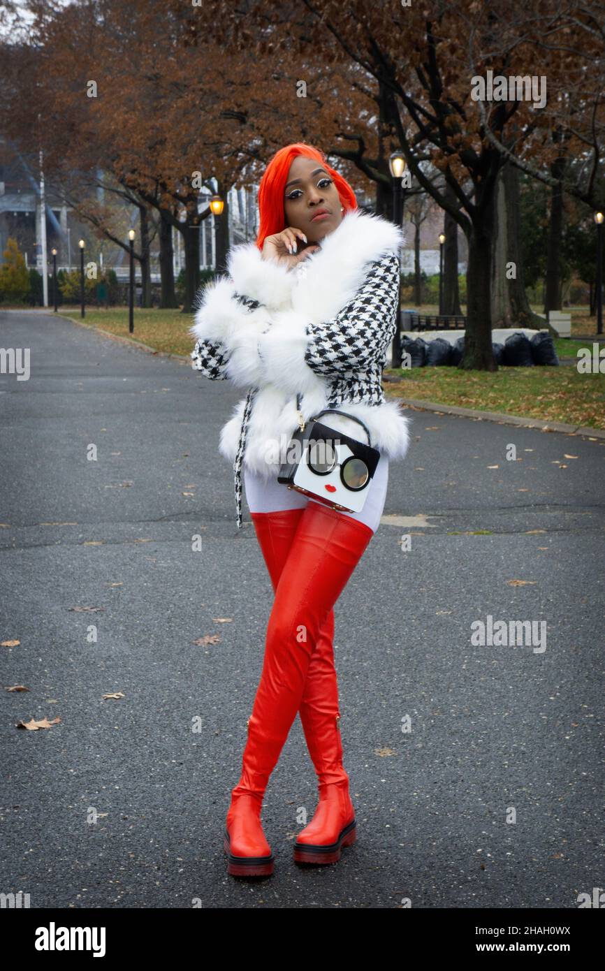 Eine attraktive Frau mit langen roten Haaren und hohen roten Stiefeln. In einem Park in Queens, New York City. Stockfoto