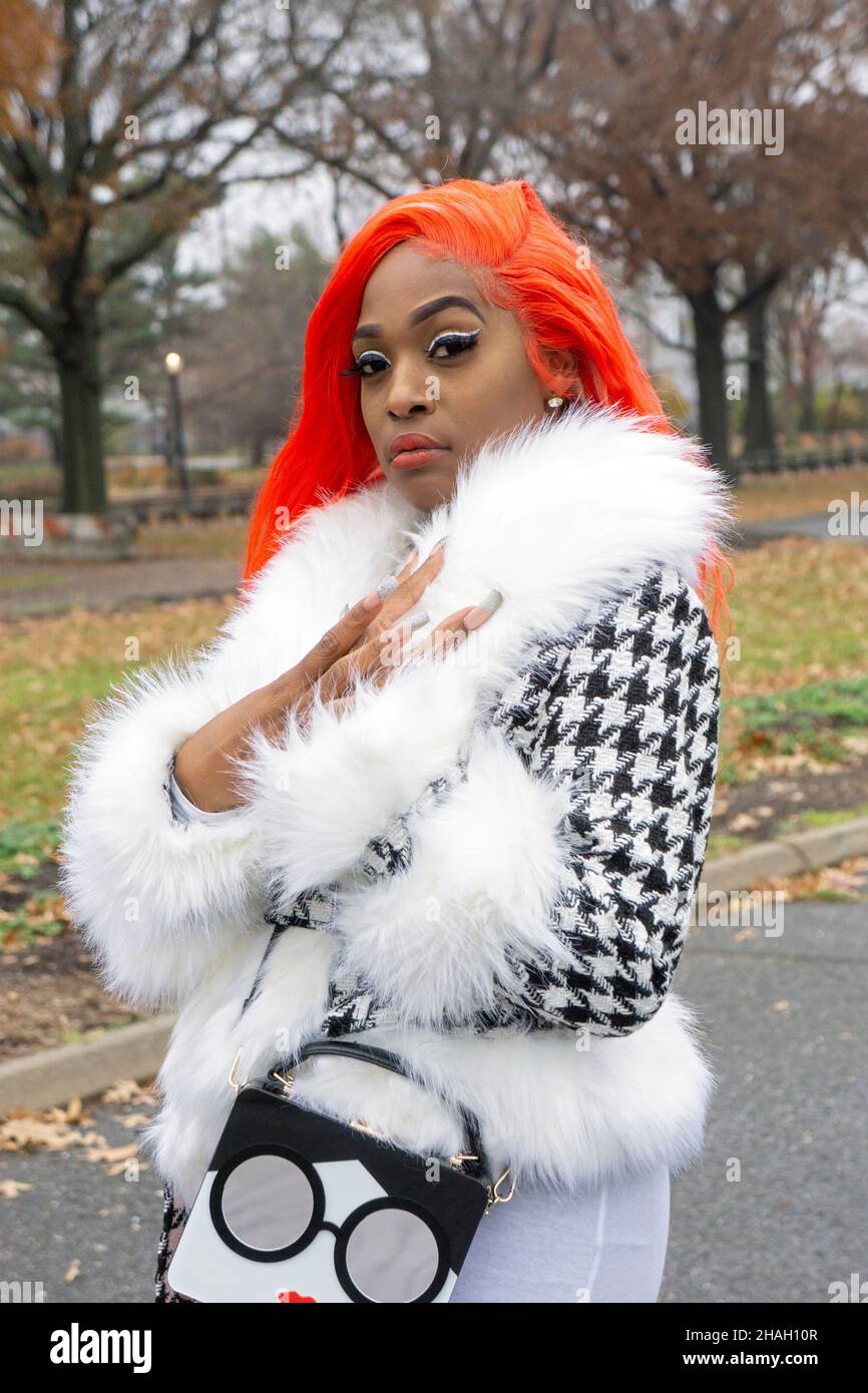Posierte Porträt einer hübschen Dame mit orangefarbenen Haaren und langen Fingernägeln. In einem Park in Queens, New York City. Stockfoto