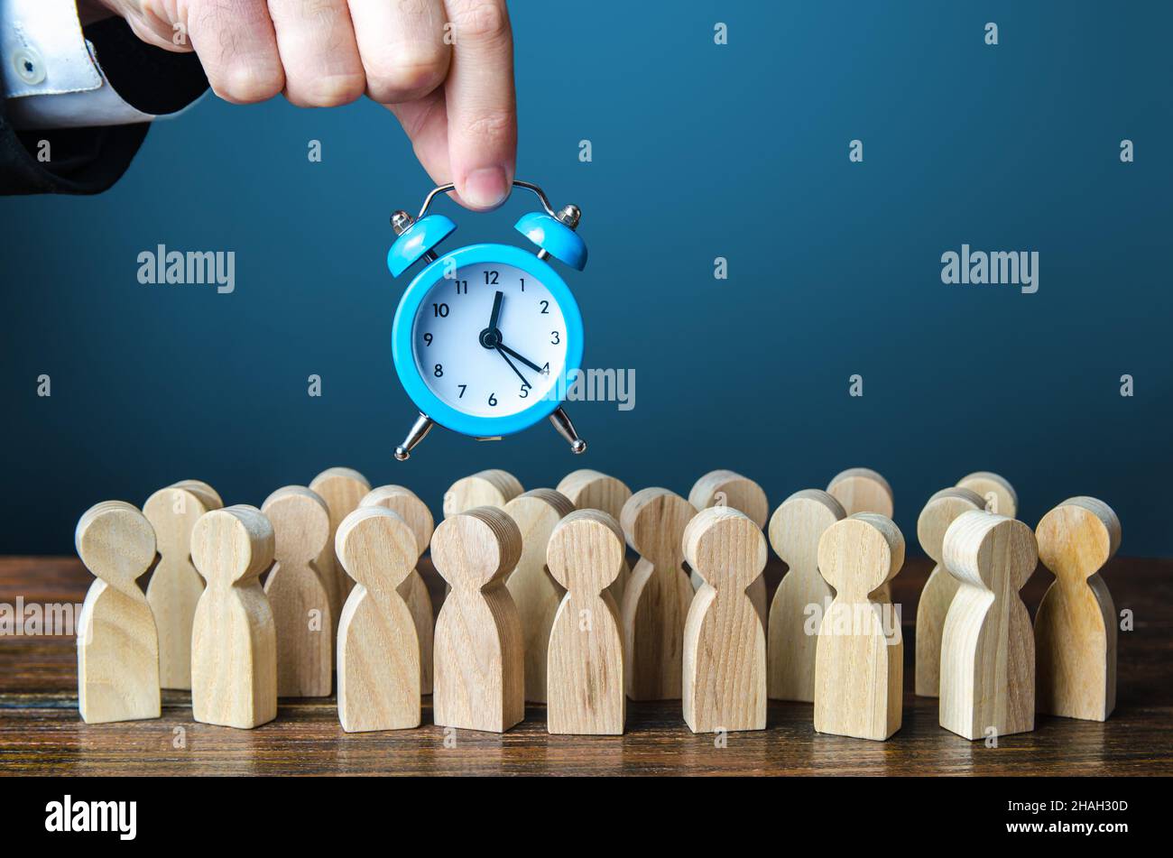 Ein Geschäftsmann hält einen Wecker über einer Menschenmenge. Zeitmanagement. Stundenlöhne, strenge Arbeitslimits und Ruhezeit. Dringend Stockfoto