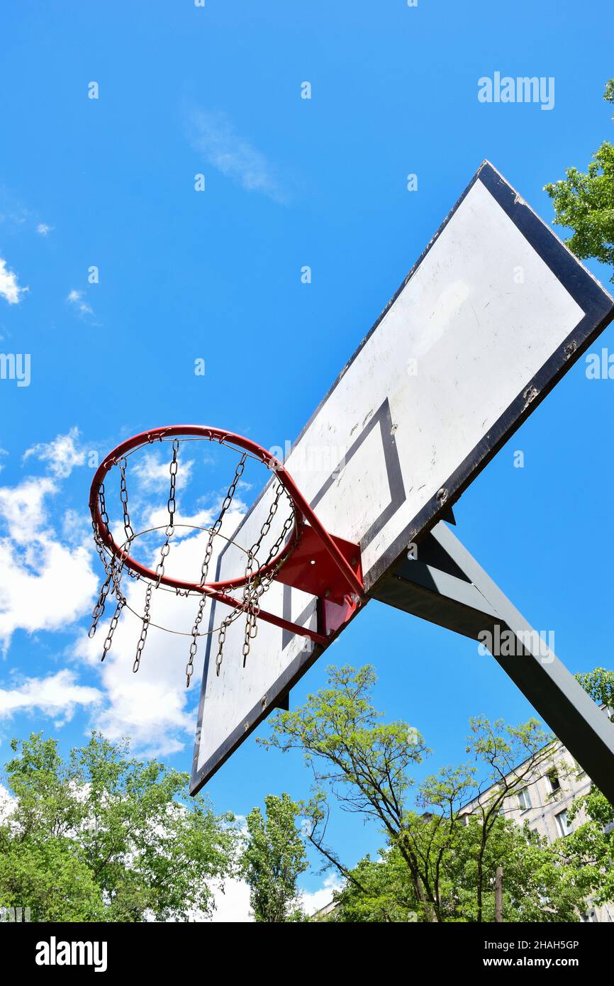 Basketballkorb und Backboard vor einem strahlend blauen Himmel mit weißen Wolken und Bäumen. Von unten aufgenommen Stockfoto