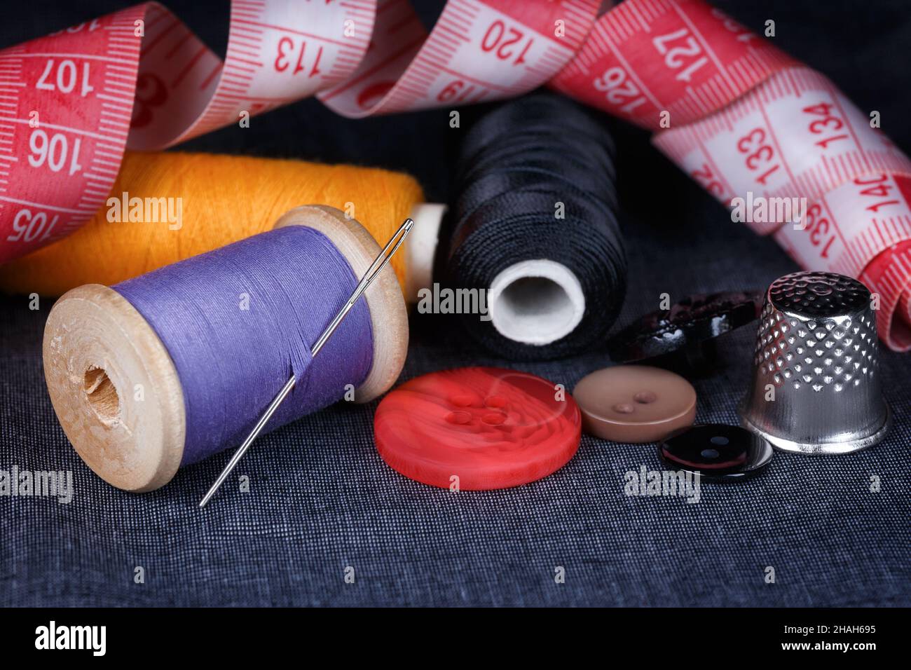 Nähen von Accessoires aus der Nähe auf Stoffbasis. Nadel, Faden, Knöpfe, Dimmel und Maßband Stockfoto
